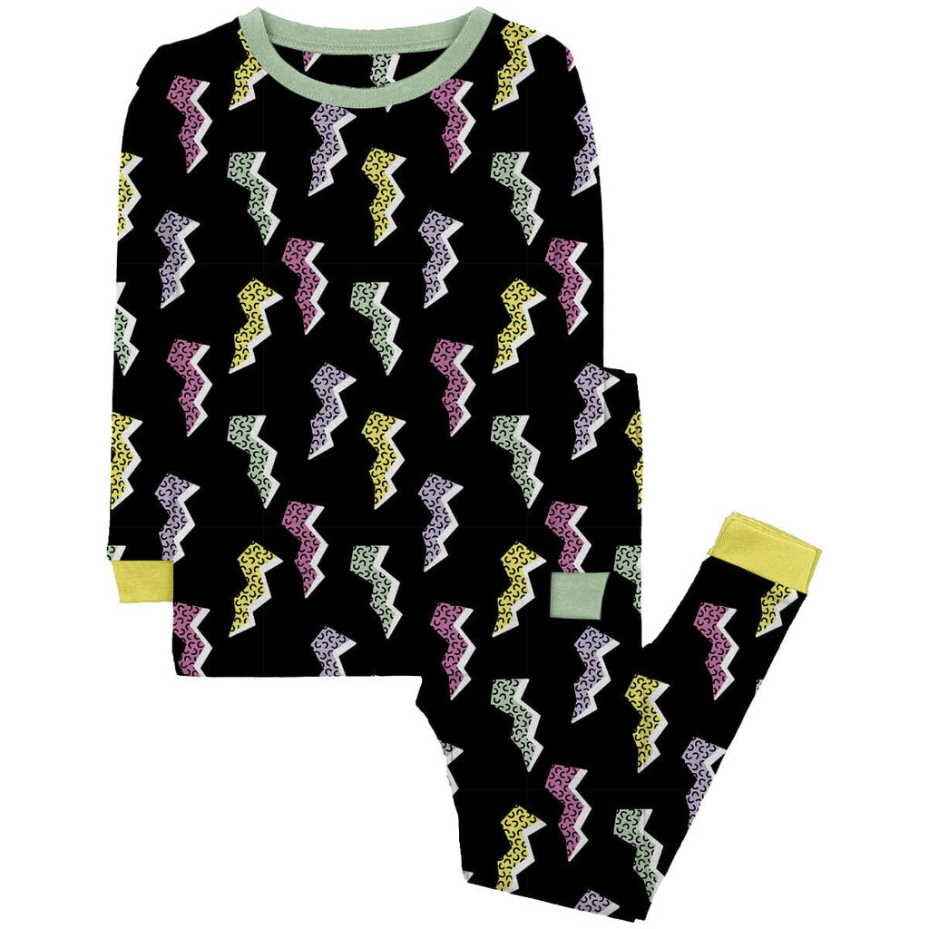 Saved By the Binky Jams Big Kids black pajama set with a vibrant lightning bolt pattern in pastel colors including yellow, green, pink, and purple. The pajama top has long sleeves with light green cuffs matching light green neckline. The pajama pants feature an elastic waistband and yellow cuffs. The set is displayed against a plain white background