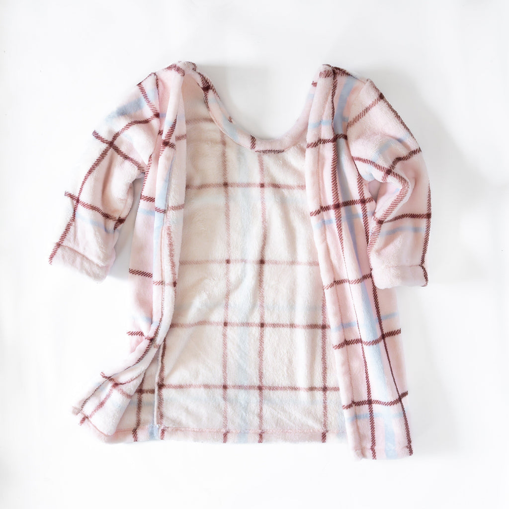 A back view of light pink/cream car seat blankie with a soft, cozy plaid pattern featuring red and blue lines. The blankie is open, showing a plush interior lining. It is laid flat against a plain white background.