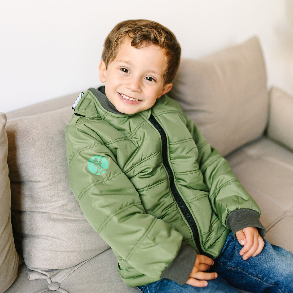 Puff/Green
Little boy with brown hair is wearing a green carseat coat.  The boy is sitting on a beige couch.  The coat is zipped up and the boy is smiling at the camera.